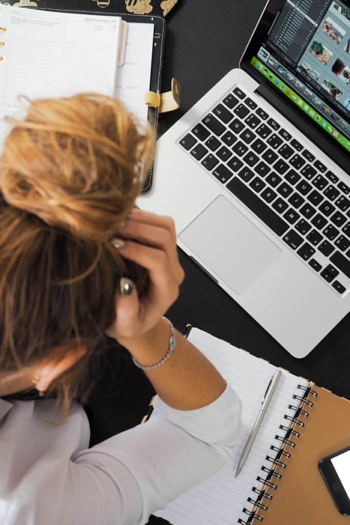 Overhead view of a stressed woman working at a desk with a laptop, phone, and notebooks.